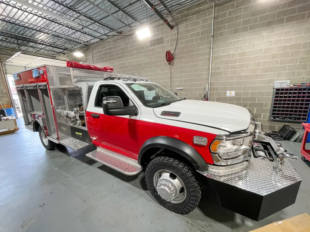 Exterior view of small fire truck showing cab, body compartments, and wheel/tire area.